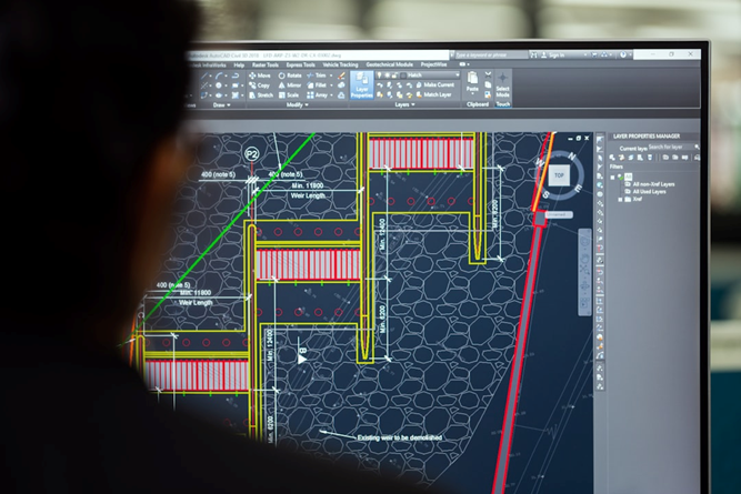 Person reviewing a detailed building design using CAD software on a computer screen, highlighting architectural and engineering elements.