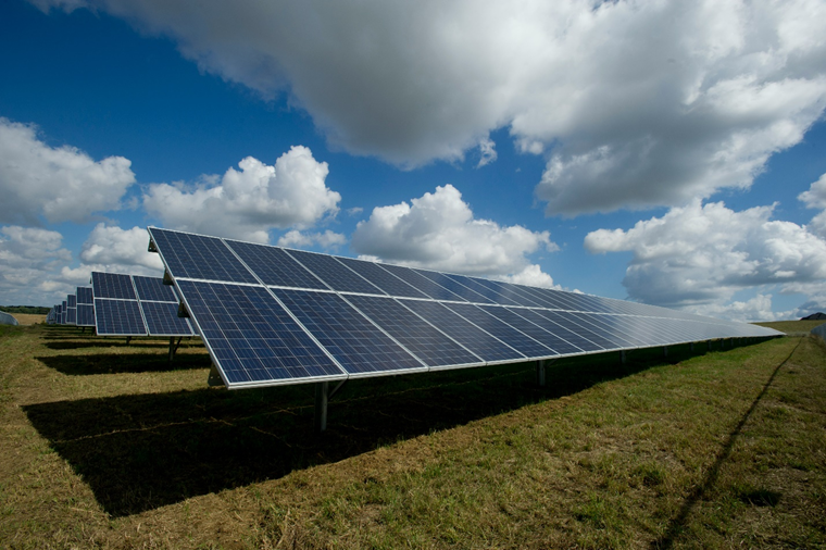 Rows of solar panels installed in an open grassy field under a partly cloudy sky, capturing renewable solar energy.